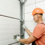A Man in an Orange Hard Hat and Safety Vest Repairs a Garage Door in Jacksonville, FL