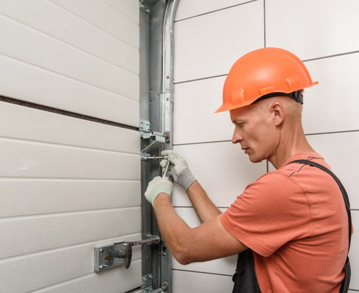 A man wearing an orange hard hat repairs a garage door during installation in Jacksonville, FL.