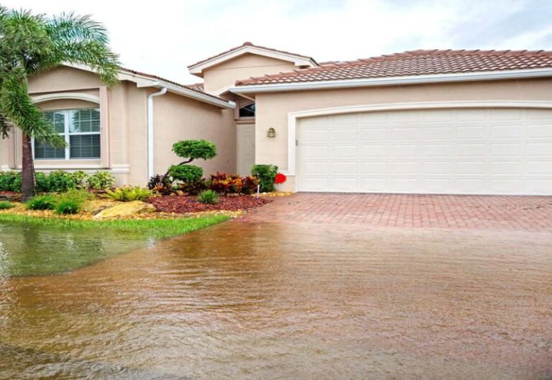 Flooded driveway in front of a beige house with red-tiled roof and palm tree in Jacksonville, FL.